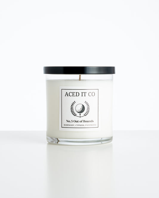Aced It Co. Out of Bounds golf-inspired candle in a glass jar with an orange golf ball label.